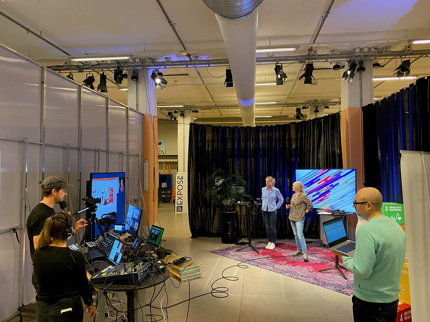 Två personer arbetar vid kamera och mixerbord, ett par personer står framför med mikrofon i handen.
